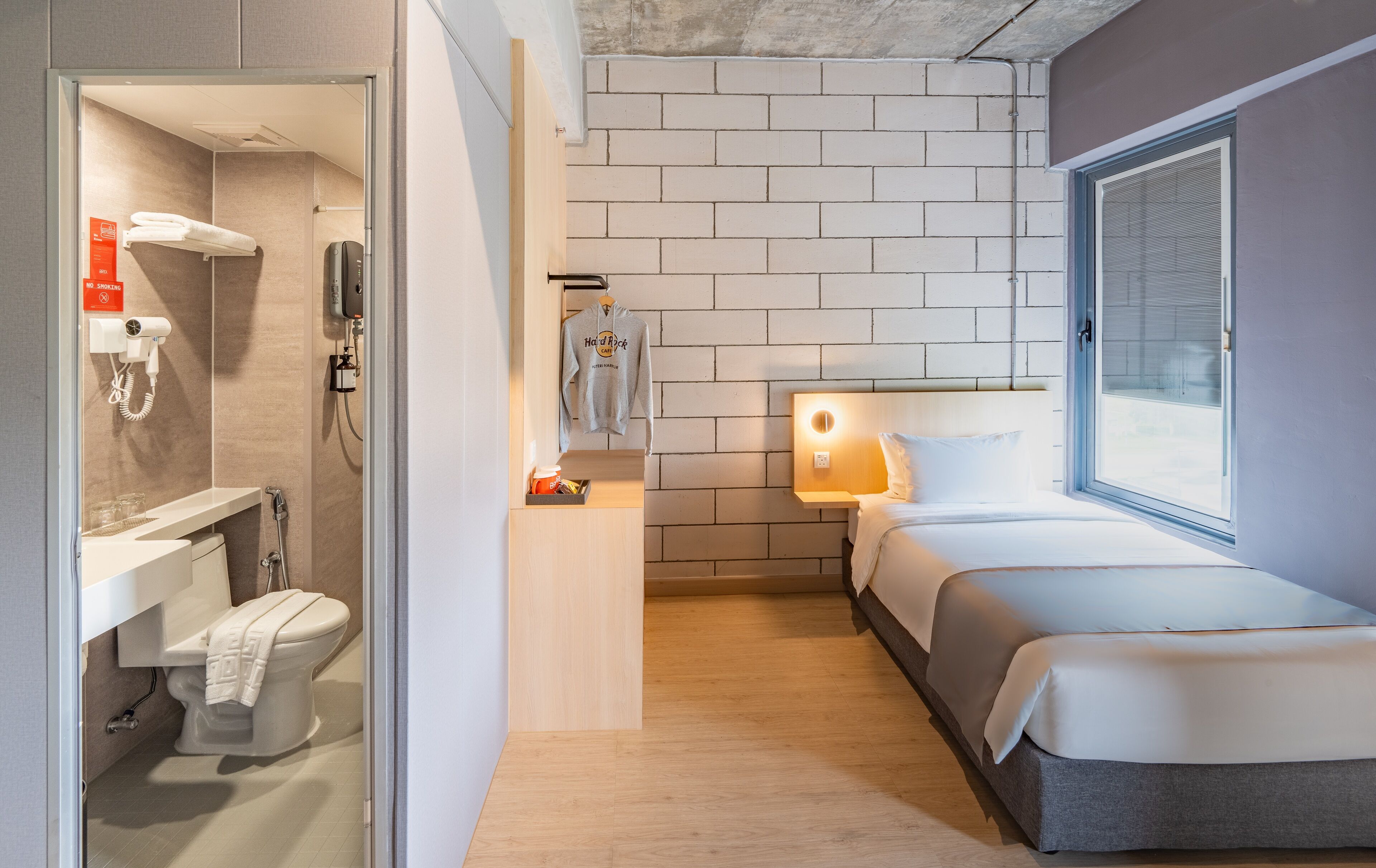 Habitación de hotel compacta con ducha, inodoro y cama con ventana.