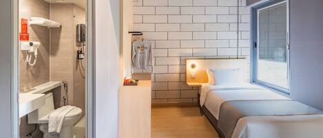 Habitación de hotel compacta con ducha, inodoro y cama con ventana.