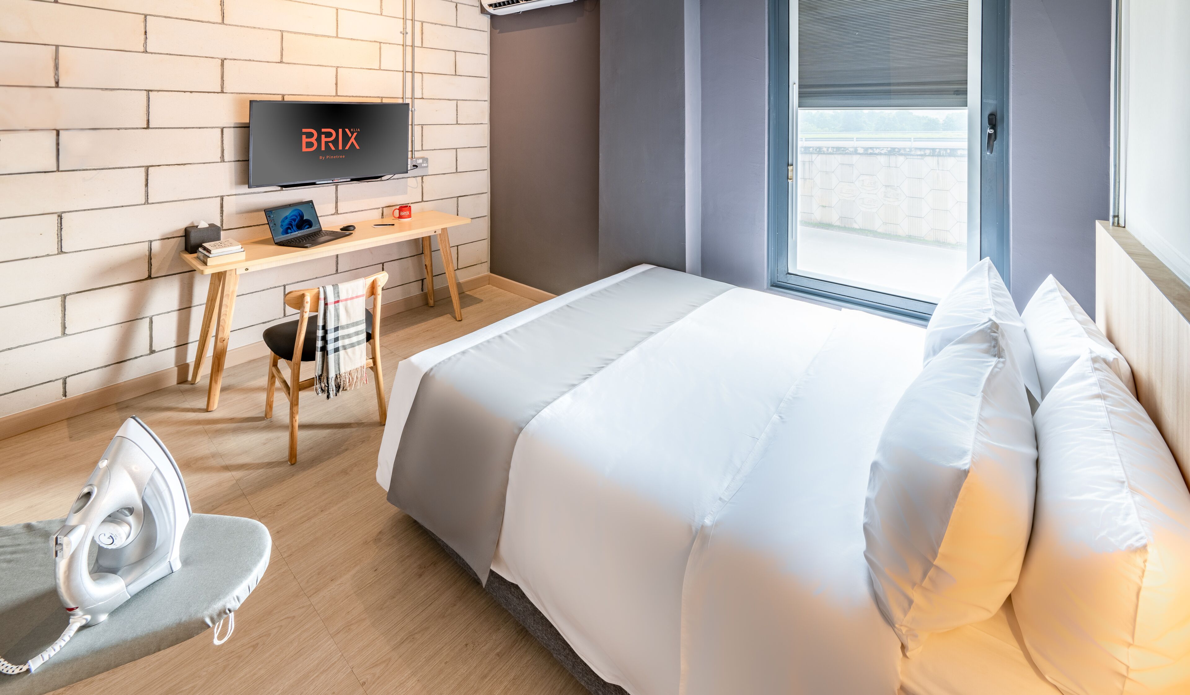 A modern hotel room with a large bed, a desk with a laptop, a chair, and a TV mounted on the wall.