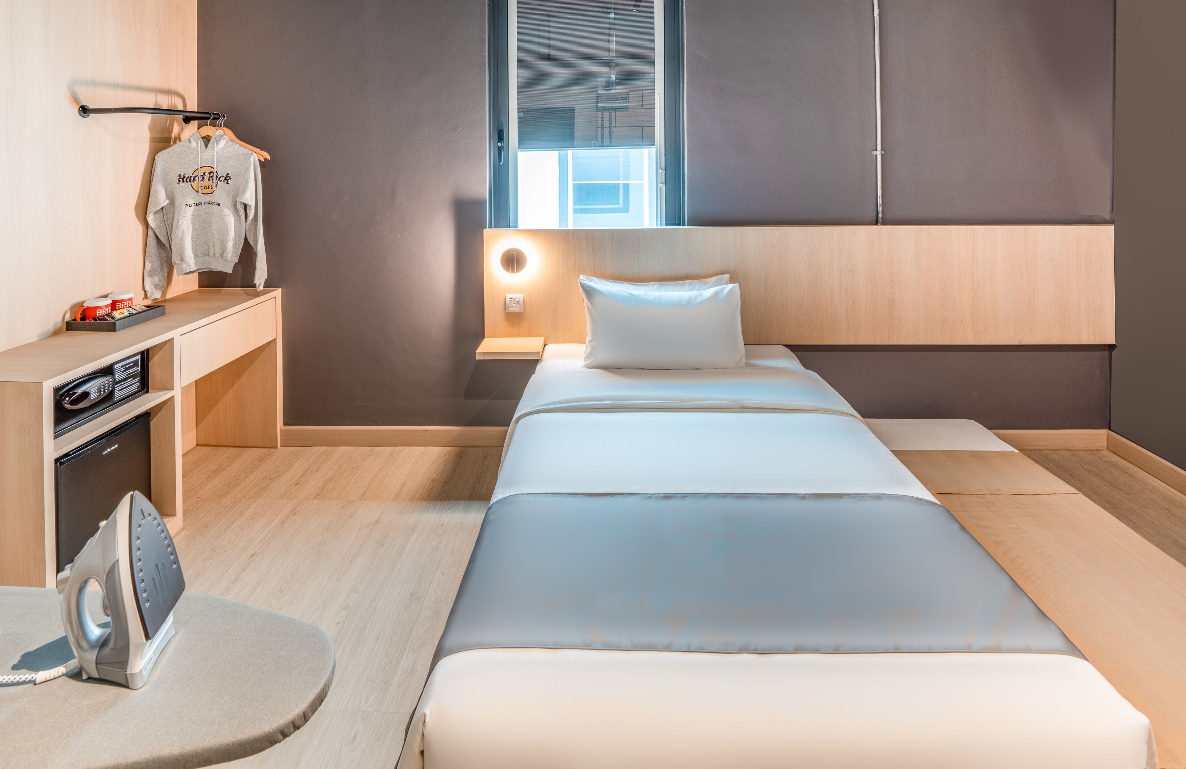 Une chambre d’hôtel comprenant un lit, une table de chevet avec une lampe, un porte-vêtements et une petite planche à repasser.