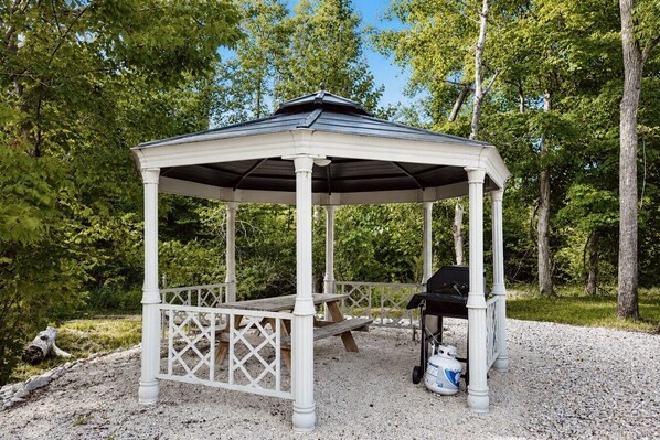 En lusthus med en bänk och en grill, omgivet av träd.