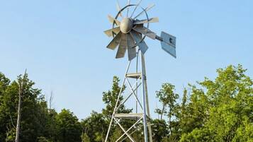 A windmill with a metal structure and blades, located near a body of water and surrounded by trees.