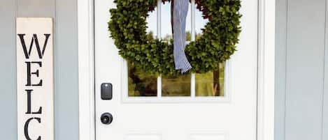 A white front door with a wreath and a 'WELCOME' sign above it.