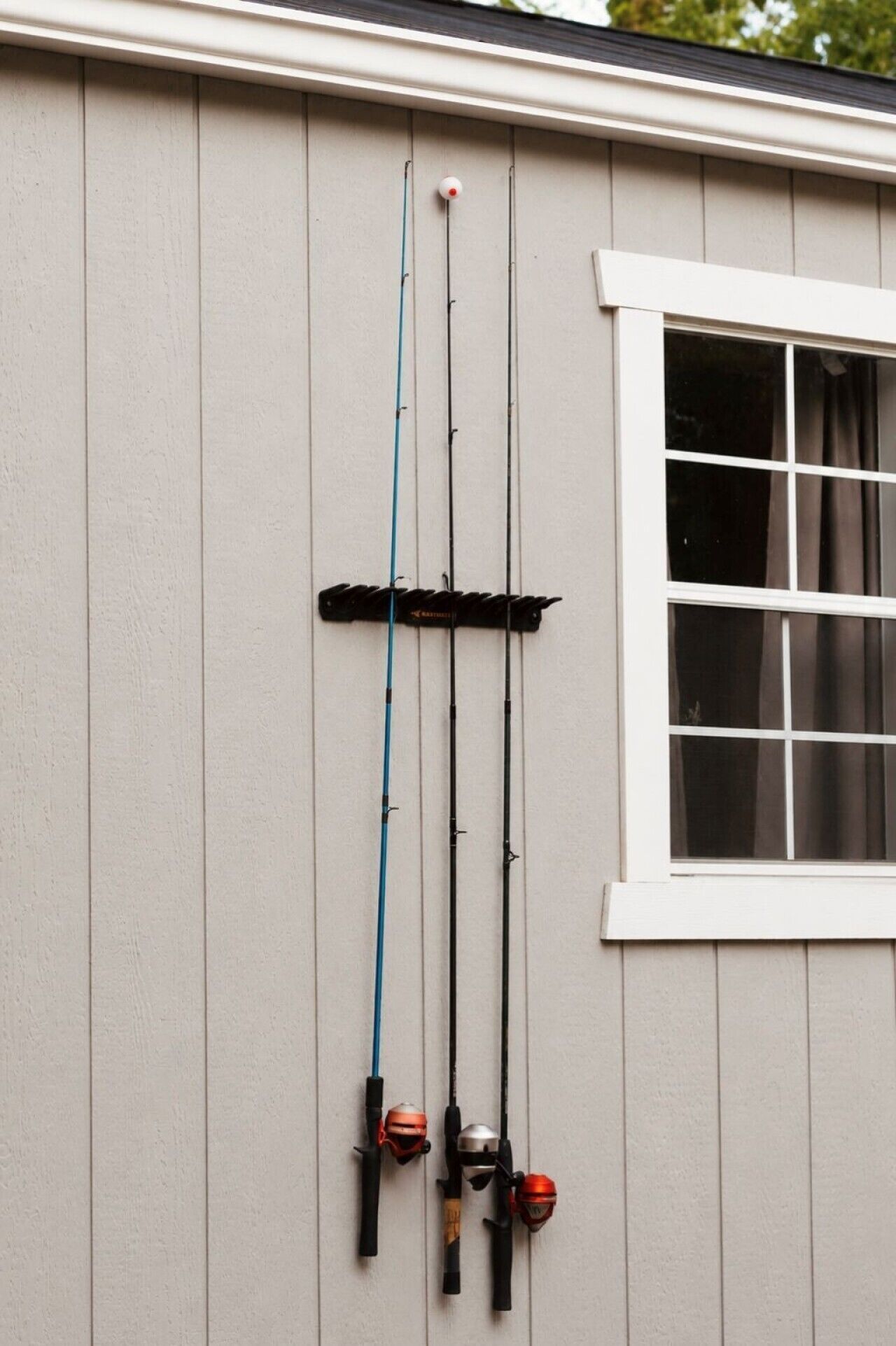 A fishing rod rack mounted on a wall with three fishing rods and two reels.