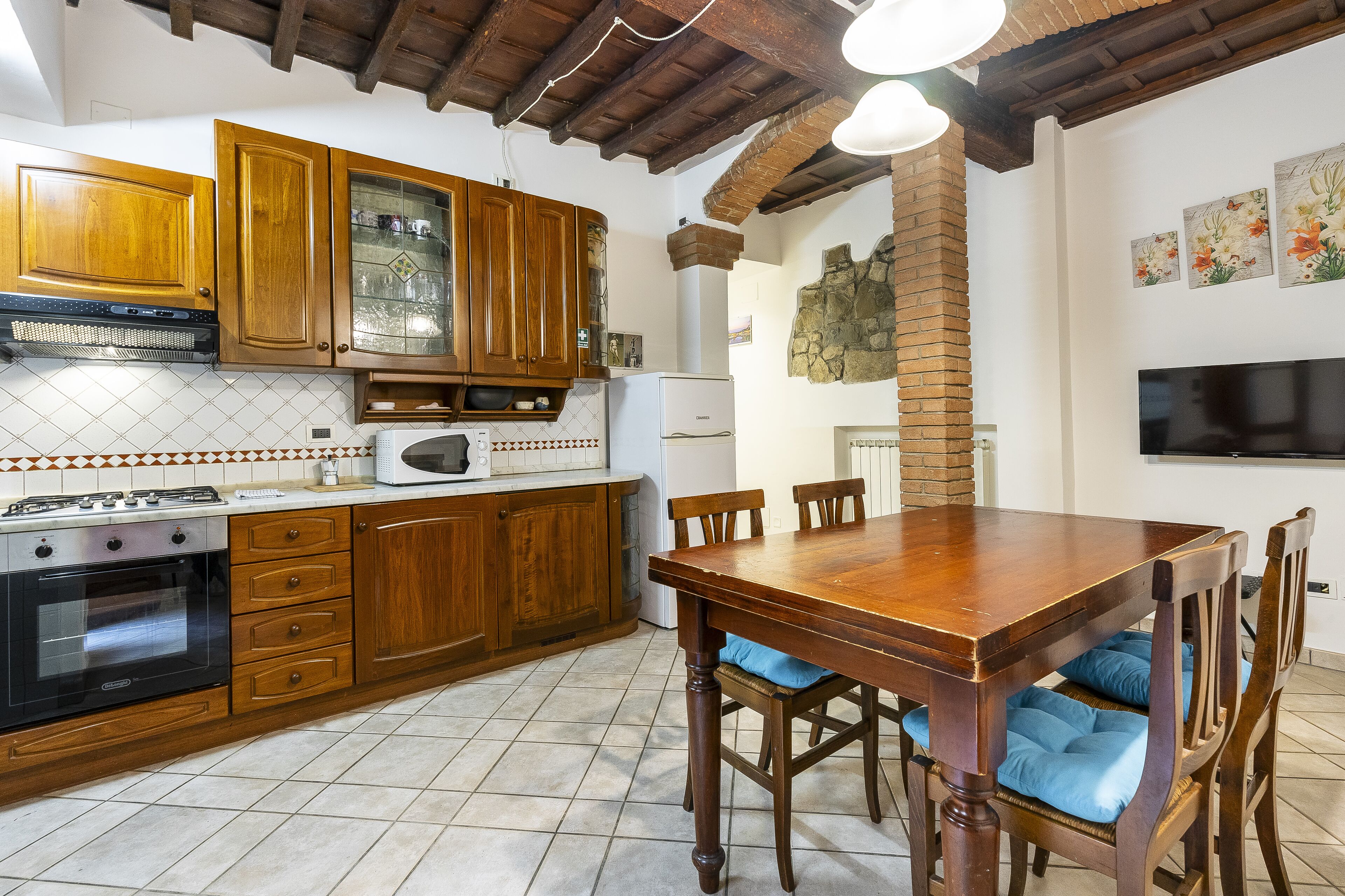 Une cuisine avec des meubles en bois, un fourneau et une table à manger agrémentée de coussins bleus.