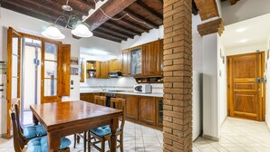 Una cocina con armarios de madera, una mesa de comedor con sillas y un pilar de ladrillo.