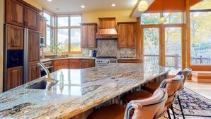 A spacious kitchen with wooden cabinets, a granite island, and a large window offering a view of the outdoors.