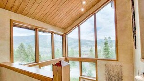 A room with large windows, wooden ceiling, and a view of a mountainous landscape.