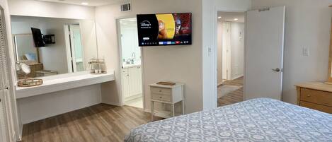 A bedroom with a bed, a dresser, a vanity with a mirror, and a television mounted on the wall.
