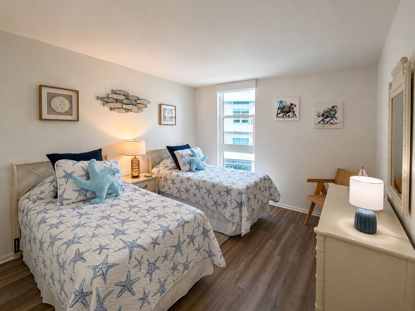 Een slaapkamer met twee bedden, een nachtkastje, een lamp, een kast en een raam met uitzicht op gebouwen.