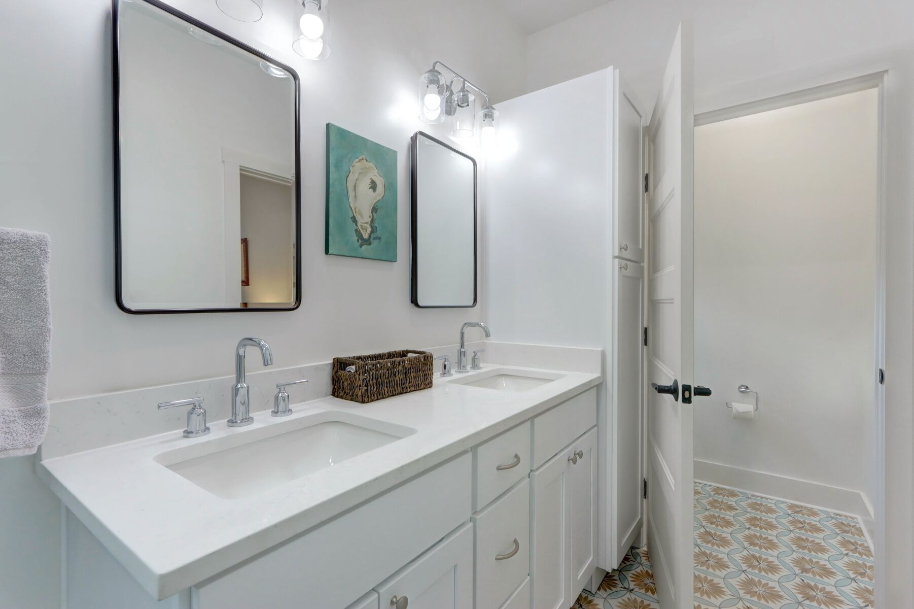 Une salle de bain avec deux lavabos, un miroir et une porte donnant sur une autre pièce.