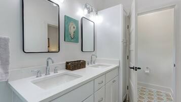 Une salle de bain avec deux lavabos, un miroir et une porte donnant sur une autre pièce.