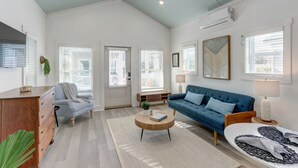 Ein geräumiges Wohnzimmer mit hoher Decke, einem blauen Sofa, einem Holztisch und einem gestreiften Sessel.