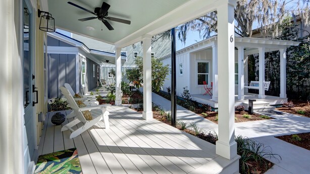 A covered porch with white columns, a ceiling fan, and outdoor seating. - Charming Tiny Cottage, 5min to SAV, 15min to Beach by Lucky Savannah (Thunderbolt)