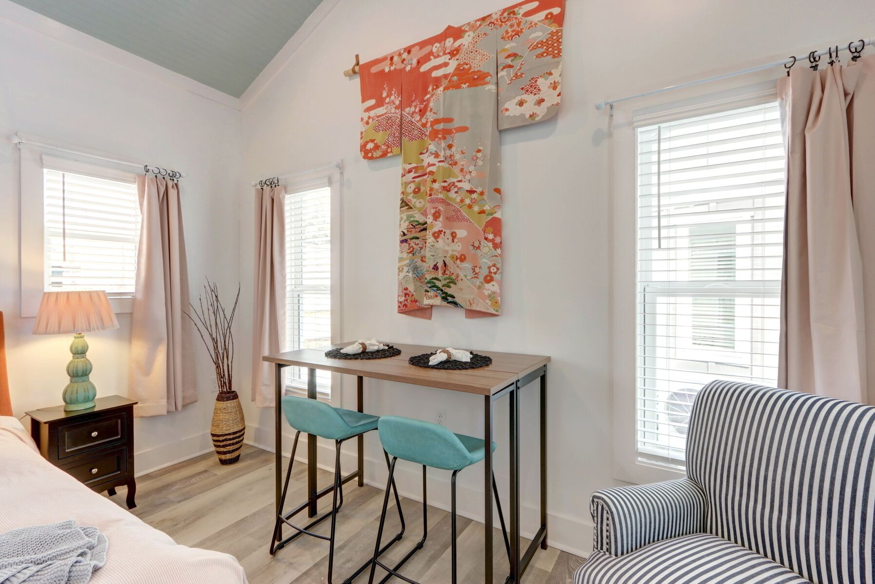 A modern room with a bed, a desk with two chairs, a striped armchair, and a large decorative tapestry.