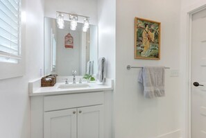 Een badkamer met een witte wastafel, een spiegel met verlichting, een handdoekhouder en een schilderij aan de muur.