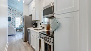 A modern kitchen with white cabinets, a stainless steel refrigerator, a built-in oven, and a coffee maker. - Marsh Hen Den - 5 Min to SAV / 15 to Beach by Lucky Savanah (Thunderbolt)