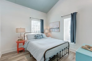 Un dormitorio con cama, dos mesitas de noche, una lámpara de noche, una ventana con cortinas y un cuadro en la pared.