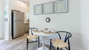 A modern kitchen with white cabinets, a stainless steel refrigerator, and a dining area with a round table and two chairs. - Marsh Hen Den - 5 Min to SAV / 15 to Beach by Lucky Savanah (Thunderbolt)