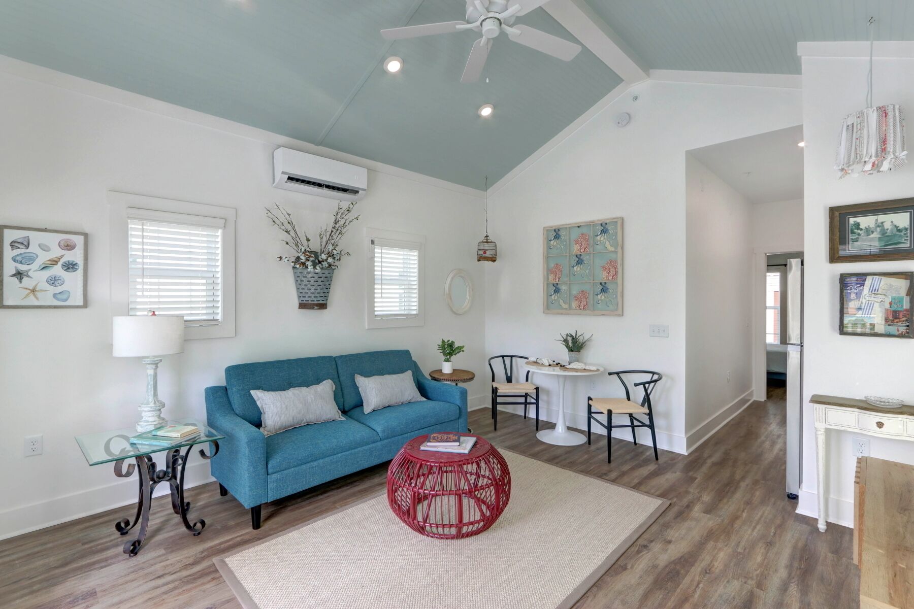 A living room with a blue sofa, a red round table, and a ceiling fan.