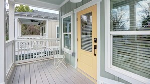 A covered porch with white railings and a yellow door, featuring a ceiling fan and a window with blinds. - Coastal Grandma Cottage - 5 min to SAV, 15 to Beach By Lucky Savannah (Thunderbolt)
