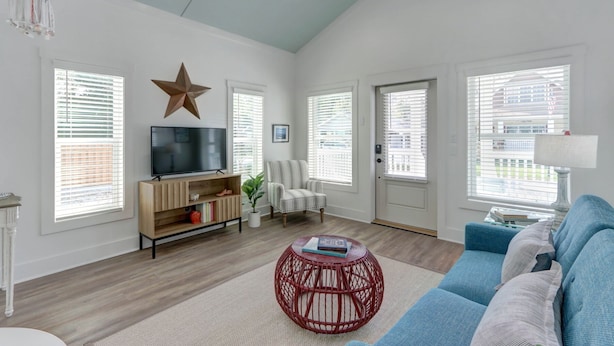 A spacious living room with a large TV, a star decoration, a blue sofa, and a red wicker coffee table. - Coastal Grandma Cottage - 5 min to SAV, 15 to Beach By Lucky Savannah (Thunderbolt)
