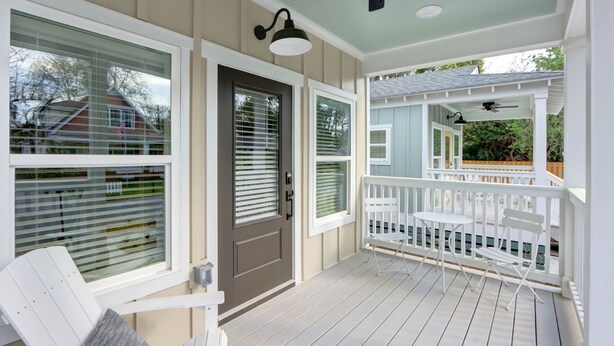 A covered porch with a ceiling fan, white railings, and a door with a window.