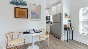 A modern kitchen with white cabinets, a stainless steel refrigerator, and a dining area with a round table and two chairs.