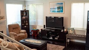 A living room with a large flat-screen TV, a brown leather armchair, a small coffee table, and a bookshelf.