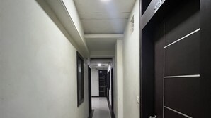 A long, narrow hallway with a black door on the right and a white door at the end. - Hotel Tushar Residency (Mathura)