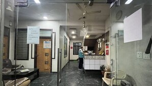 A hotel reception area with a reception desk, a waiting area with chairs, a glass partition, and a ceiling fan. - Hotel Tushar Residency (Mathura)