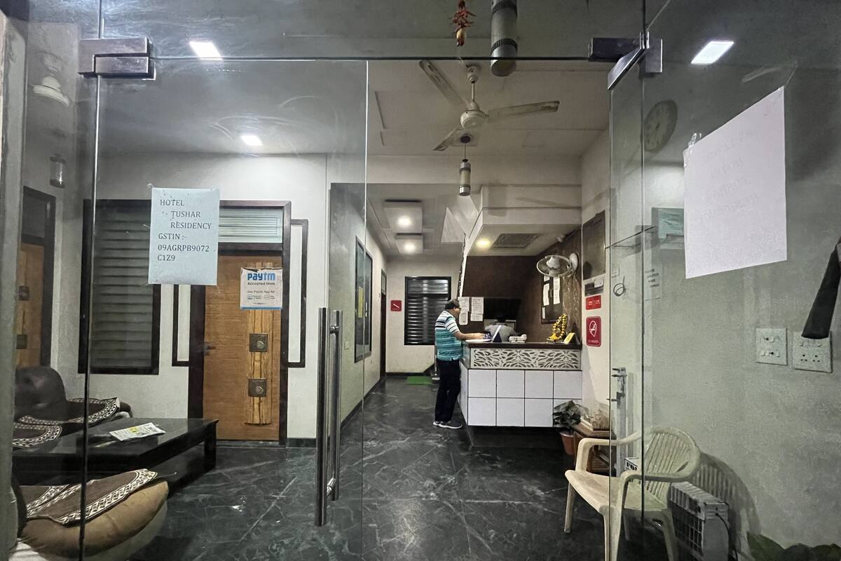 A hotel reception area with a reception desk, a waiting area with chairs, a glass partition, and a ceiling fan.