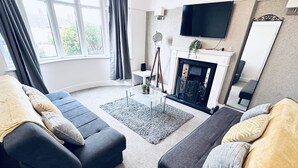 Ein modernes Wohnzimmer mit zwei grauen Sofas, einem Kamin, einem Flachbildfernseher und einem großen Fenster mit Vorhängen.