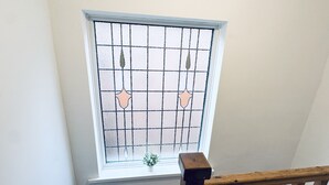 Ein Fenster mit Gittermuster und Verzierungen, ein hölzernes Geländer und eine kleine Pflanze im Fensterbrett.
