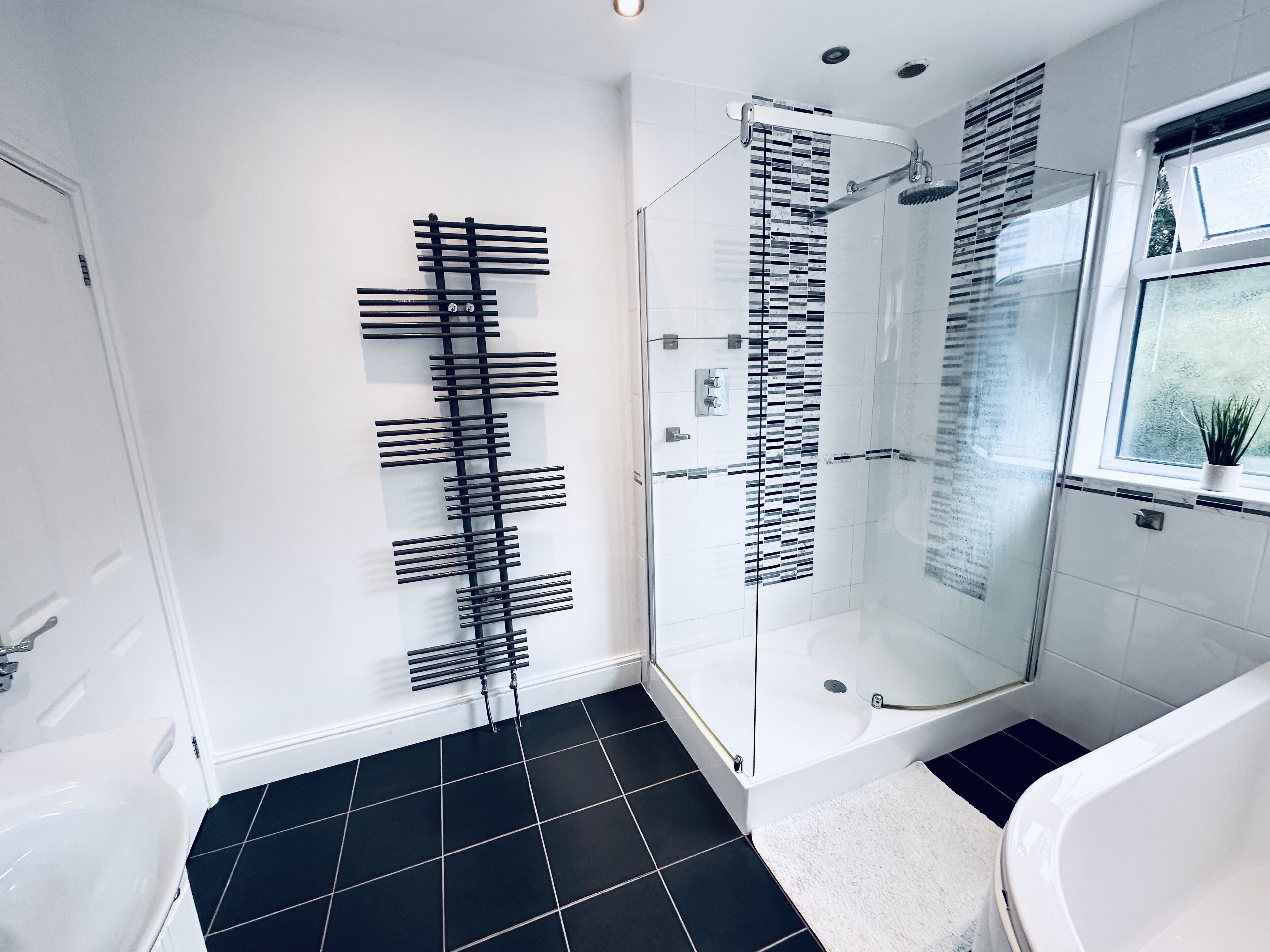 A modern bathroom with a glass shower enclosure, a black and white tiled floor, and a white bathtub.