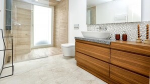 Un baño moderno con un espejo grande, un lavabo blanco, muebles de madera y una cabina de ducha de vidrio.