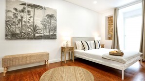 Un dormitorio moderno con una cama grande, un tapete redondo tejido, un banco y dos lámparas fijadas a la pared.