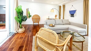 A modern living room with a sofa, a glass coffee table, a rattan chair, and a potted plant. - Green Algarve Gem Spacious 2 BDR By Misha s Place (Faro)