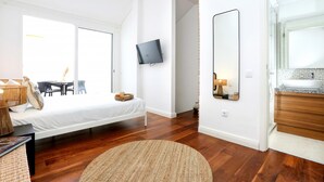 Ein modernes Schlafzimmer mit Bett, Fernseher, großem Spiegel und einem Badezimmer mit Waschbecken und Waschtisch.