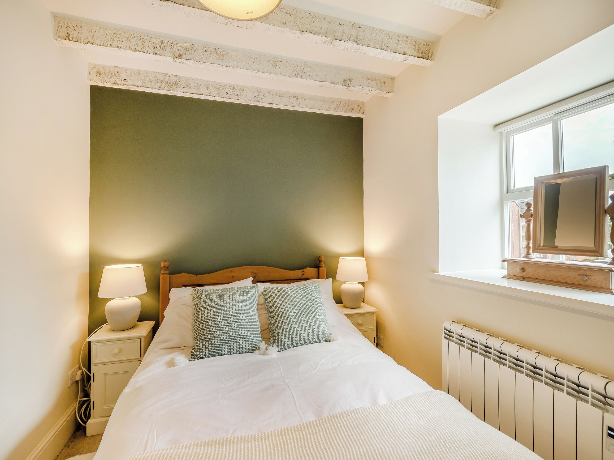 A bedroom with a bed, two bedside lamps, a nightstand, a window with a view, and a radiator.