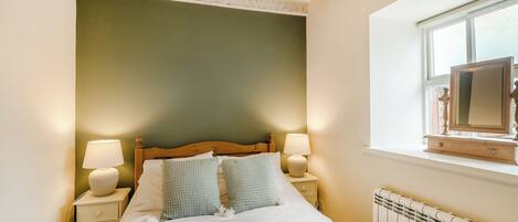 A bedroom with a bed, two bedside lamps, a nightstand, a window with a view, and a radiator.
