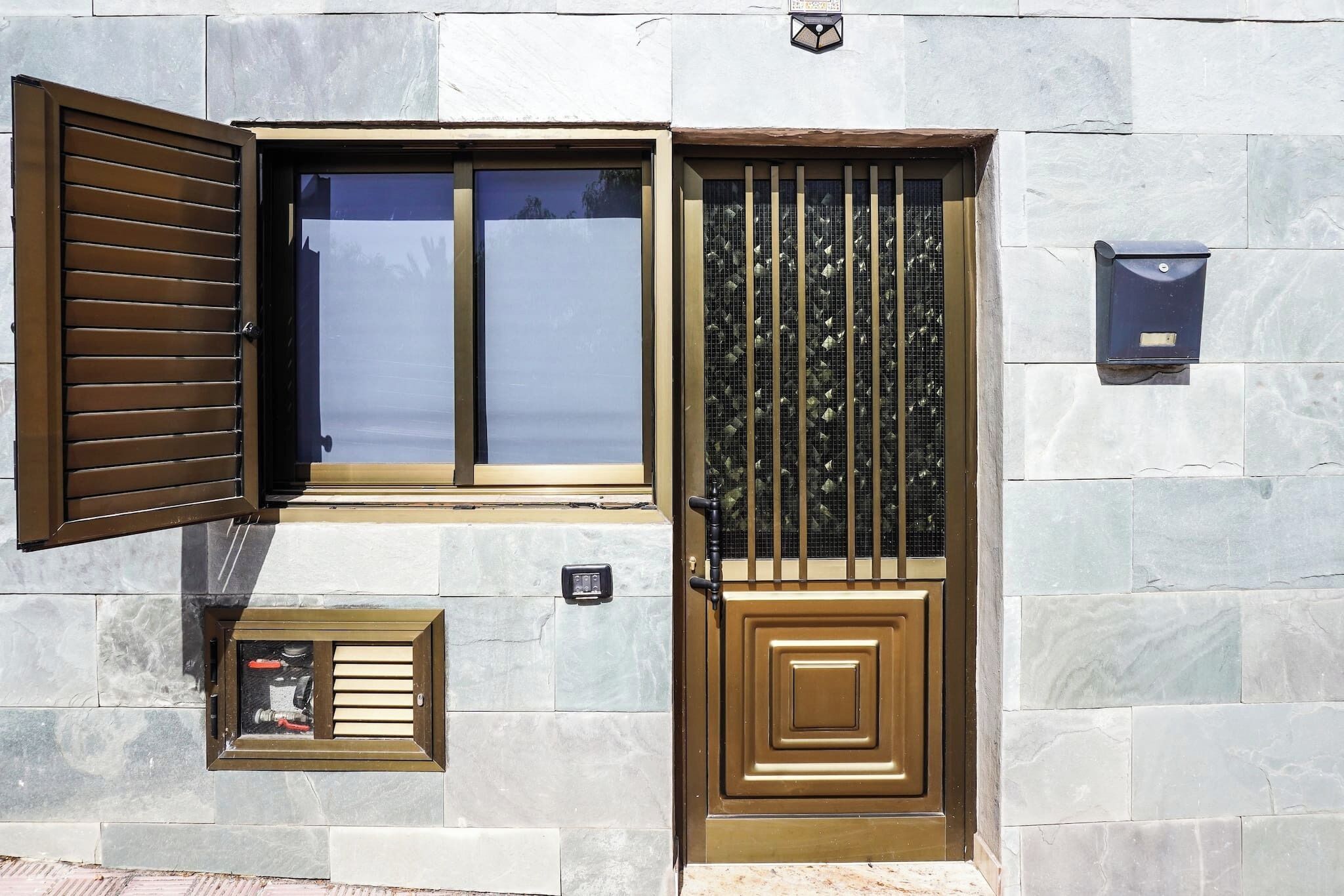 Une entrée d’immeuble avec une porte en métal, une fenêtre avec des stores et une boîte aux lettres.