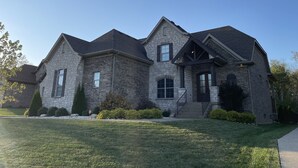A large stone house with a steeply pitched roof, multiple chimneys, and a well-maintained lawn.