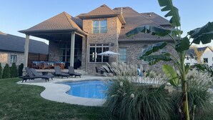 A two-story house with a covered patio, a swimming pool, and a well-maintained lawn.