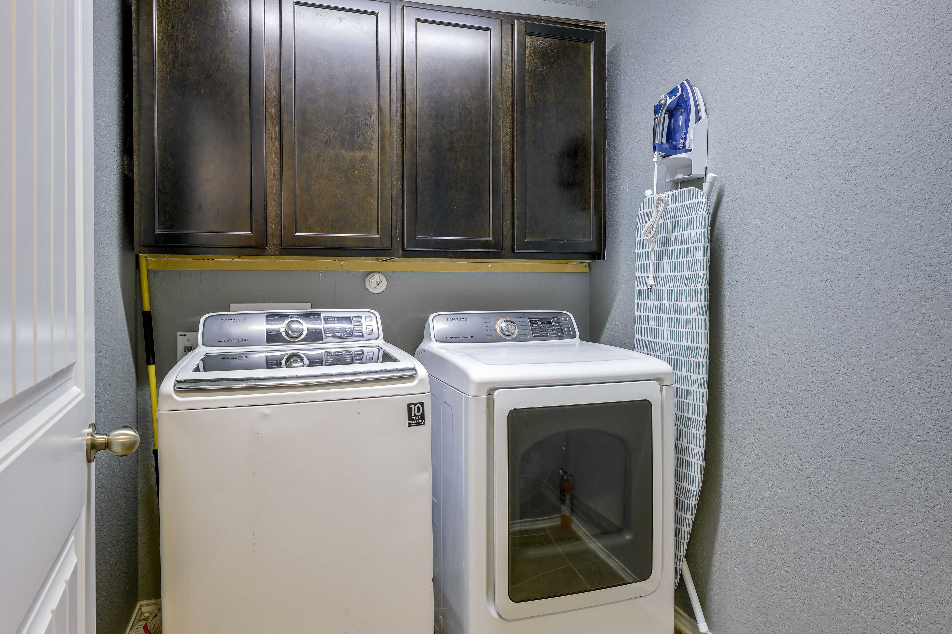 A laundry room with two washers and a dryer, a cabinet above, and a towel rack on the wall.