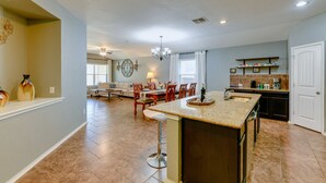 A spacious kitchen with a central island, a dining area with a chandelier, and a living room with a sofa and decorative wall art.