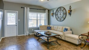 A living room with a beige sofa, a glass coffee table, a ceiling fan, and a decorative wall piece.