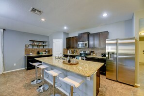 Una cocina moderna con encimeras de granito, electrodomésticos de acero inoxidable y una isla central con taburetes de bar.