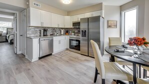 A modern kitchen with white cabinets, stainless steel appliances, and a dining area with a table set for two. - North Myrtle Beach Oasis w/ Community Pool! (North Myrtle Beach)