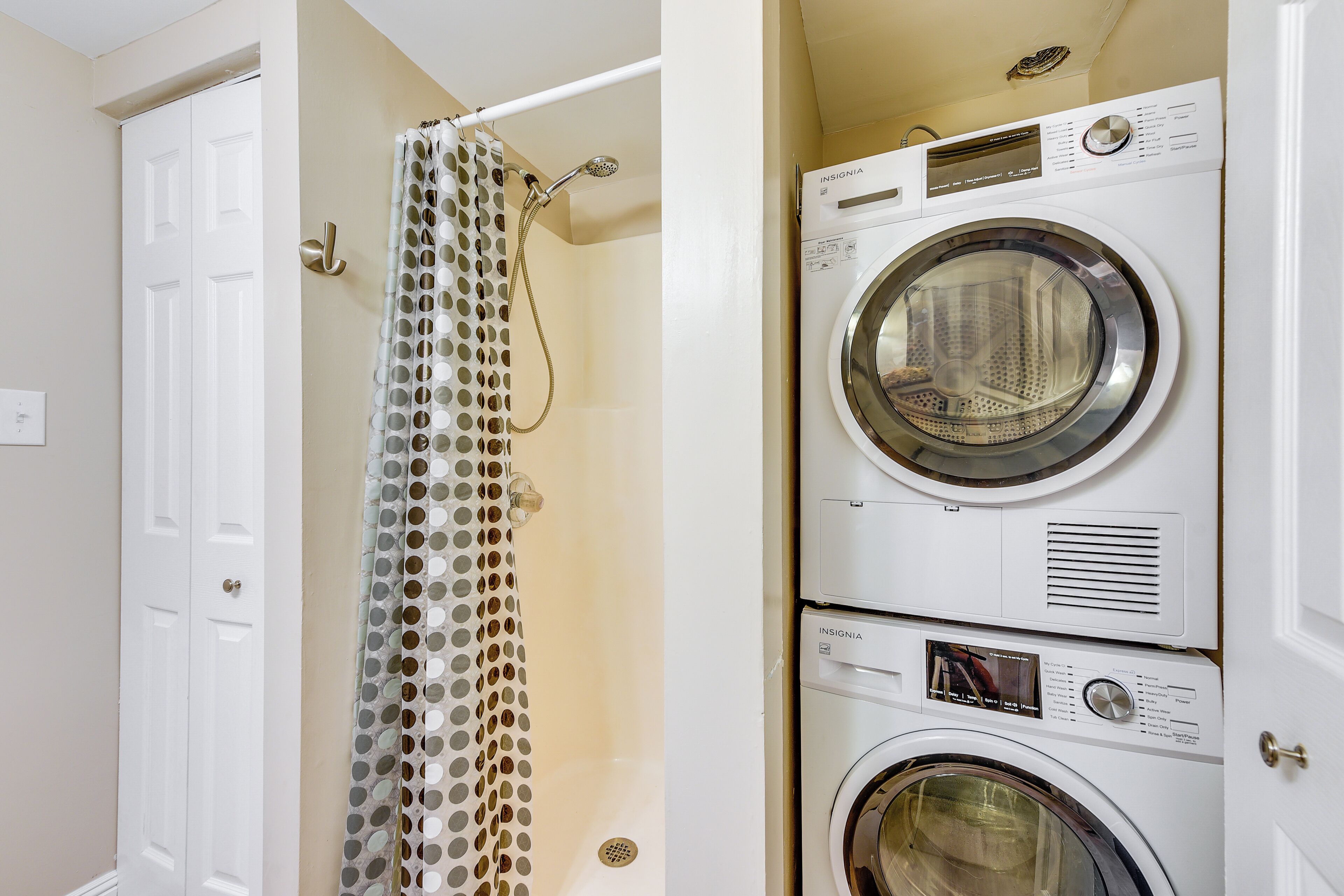 A laundry area with two stacked washing machines and a shower curtain.